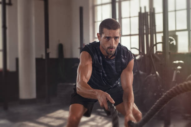 A focused, athletic man doing battle rope exercises in a gym, pushing through the challenges of cardio after an intense leg day.