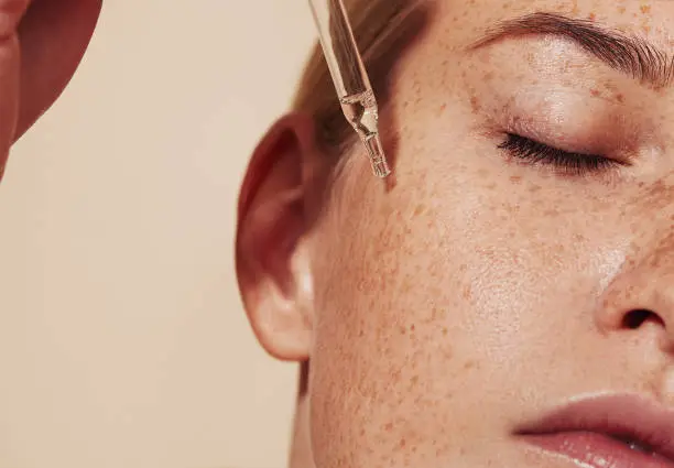 A close-up of a woman’s face with freckles, as a serum is applied to help fade them.