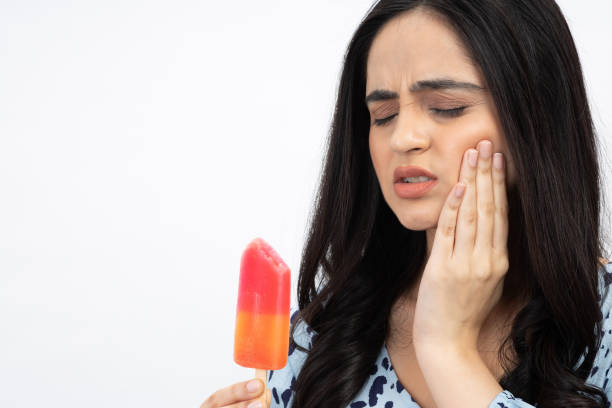 A woman holding an ice pop and touching her cheek, showing discomfort due to tooth sensitivity.