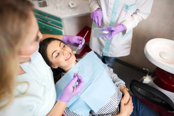 Woman smiling during a dental check-up, attended by two dental professionals.







