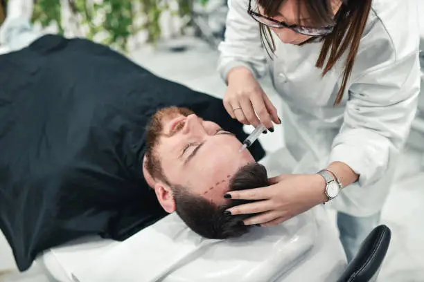 A medical professional performing forehead reduction surgery on a man lying on a chair.