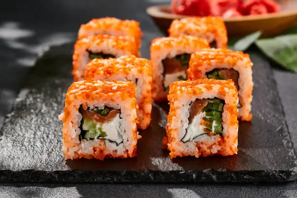 Close-up of masago sushi rolls with creamy filling, cucumber, and a vibrant orange masago coating.