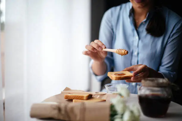 A woman spreading honey on toast using a wooden dipper, highlighting the health benefits of eating honeycomb as a natural sweetener.