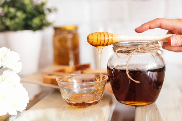 A jar of honey with a wooden dipper dripping honey into a glass bowl, showcasing the natural sweetness and health benefits of honeycomb.